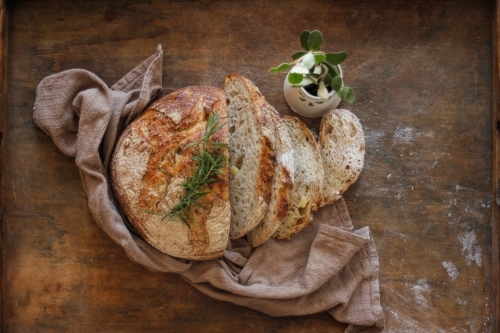 Cut sourdough on wooden tray with brown linen tea towel - Australian Stock Image