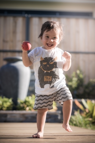 Cute 1 year old boy takes his first steps outside in his suburban backyard - Australian Stock Image