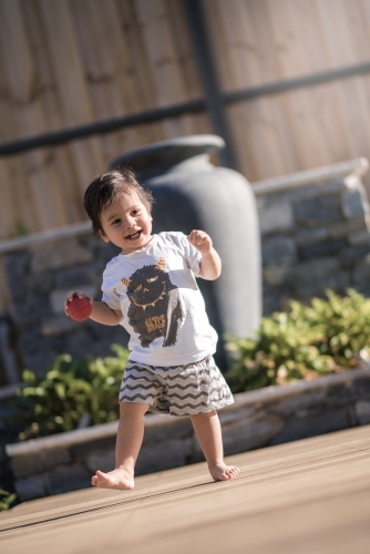 Cute 1 year old boy takes his first steps outside in his suburban backyard