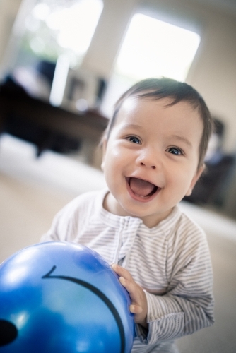 Cute 1 year old mixed race boy plays at home with a smiley face ball