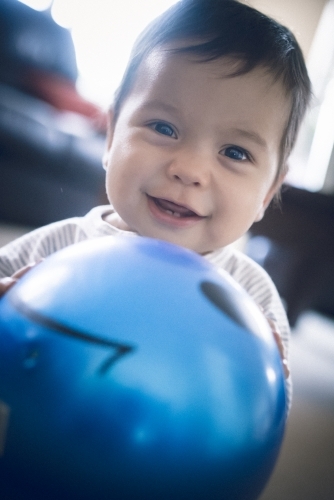 Cute 1 year old mixed race boy plays at home with a smiley face ball - Australian Stock Image