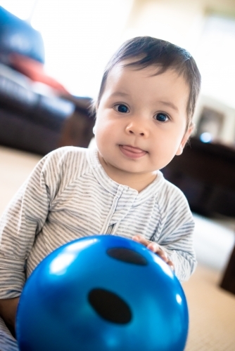 Cute 1 year old mixed race boy plays at home with a smiley face ball