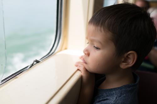 Cute 3 year old mixed race boy looks out a boat window - Australian Stock Image