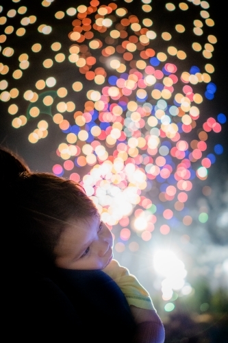 Cute mixed race baby boy cuddles his parent while new year's fireworks explode in background
