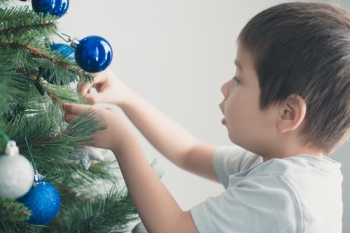 Cute mixed race boy hanging decorations on Christmas tree - Australian Stock Image
