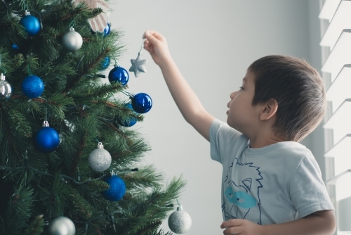 Cute mixed race boy hanging decorations on Christmas tree - Australian Stock Image