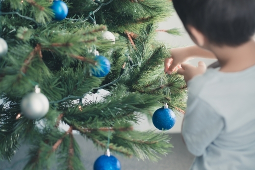 Cute mixed race boy hanging decorations on Christmas tree - Australian Stock Image