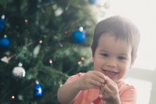 Cute mixed race boy hanging decorations on their Christmas tree - Australian Stock Image