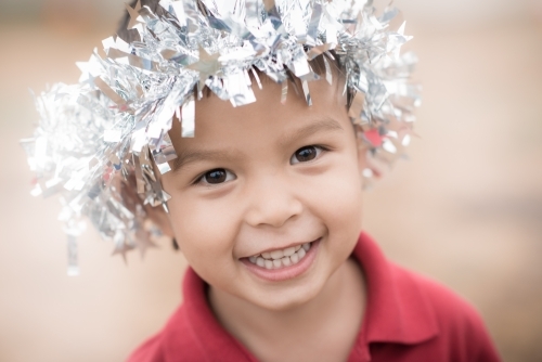 Cute mixed race boy looking angelic with Christmas tinsel on his head - Australian Stock Image