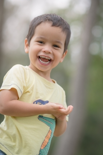 Cute mixed race boy playing in a park outside among the trees - Australian Stock Image
