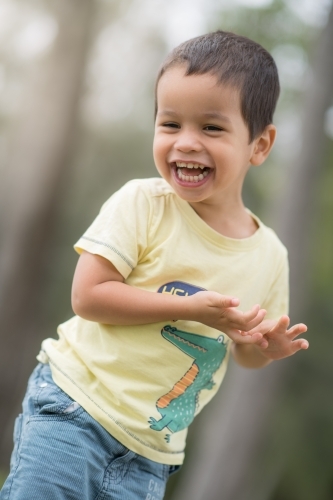 Cute mixed race boy playing in a park outside among the trees - Australian Stock Image