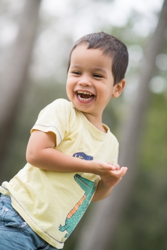 Cute mixed race boy playing in a park outside among the trees - Australian Stock Image
