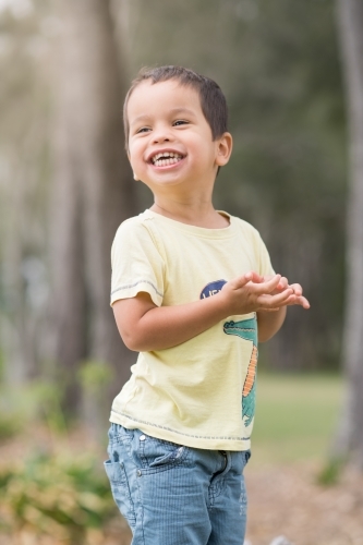 Cute mixed race boy playing in a park outside among the trees - Australian Stock Image