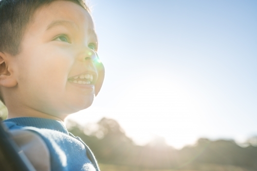 Cute mixed race three year old boy playing on a swing in a suburban playground - Australian Stock Image