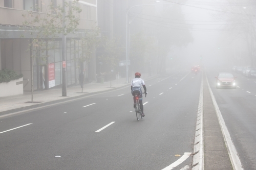 Cyclist riding down road in fog - Australian Stock Image