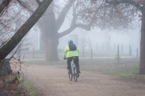 cyclist riding on a path through early morning fog - Australian Stock Image