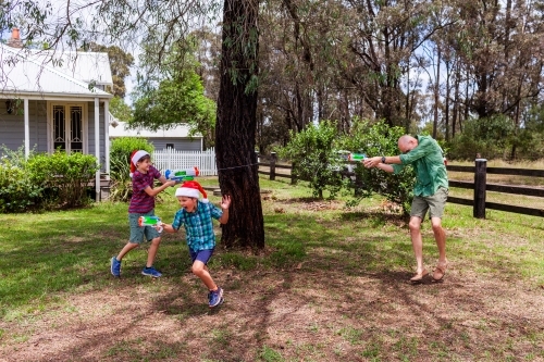 Dad and boys having water fight in front yard at Christmas - Australian Stock Image