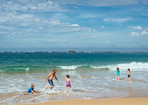 Dad and kids playing in surf - Australian Stock Image