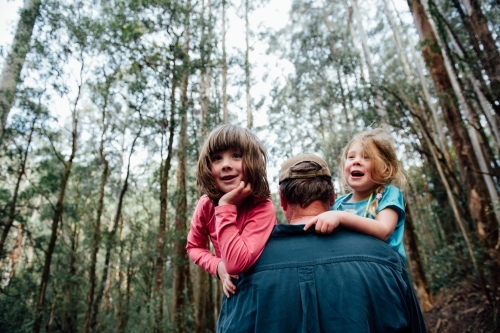Dad carrying two daughters in the forest