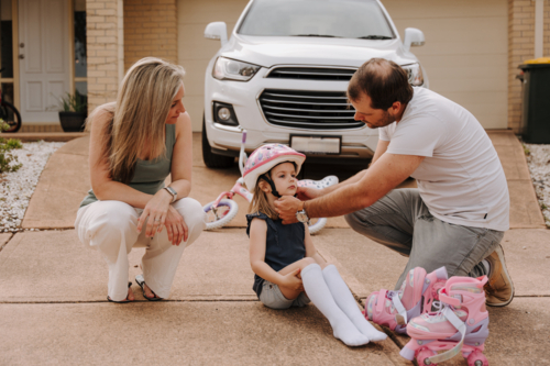Dad helping daughter fix her helmet while mum sits beside her. - Australian Stock Image