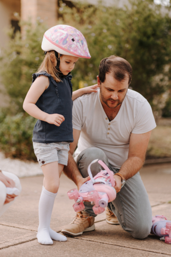 Dad helping daughter get into her roller skate gear. - Australian Stock Image