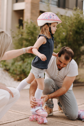 Dad helping daughter get into her roller skate gear. - Australian Stock Image