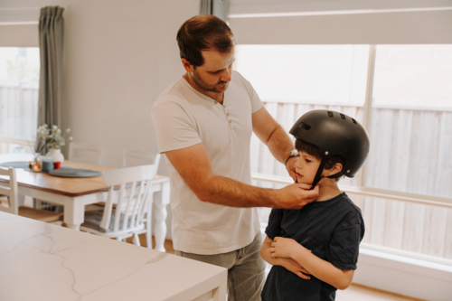 Dad helping his son put on his helmet. - Australian Stock Image