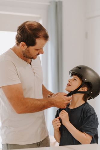 Dad helping his son put on his helmet. - Australian Stock Image