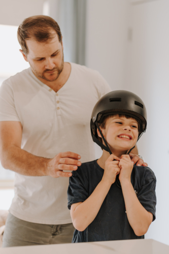 Dad helping son put on his helmet. - Australian Stock Image