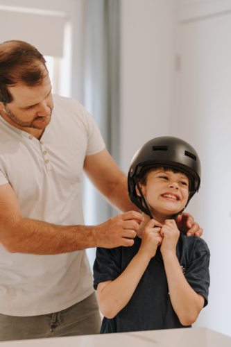 Dad helping son put on his helmet. - Australian Stock Image