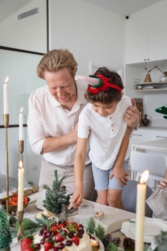 Dad helping son slice pavlova at Christmas dinner table - Australian Stock Image