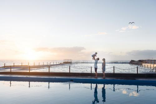 Dad throwing child in the air at sunrise over the ocean pool - Australian Stock Image