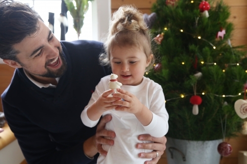 Dad with daughter looking at ornament with Christmas in background - Australian Stock Image