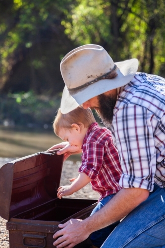 Dad with son opening treasure chest beside river