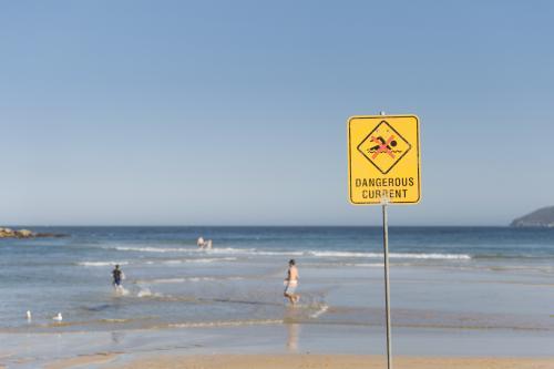 Dangerous Current Sign on the Beach with People Running In the Shallow Water - Australian Stock Image