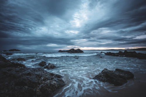 dark storm clouds over rocks on ocean shore on south coast - Australian Stock Image