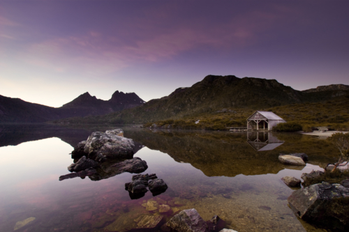 Dawn light reflects across the still waters of Dove Lake beneath Cradle Mountain - Australian Stock Image