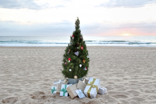 Decorated Christmas tree with presents at sunrise on beach