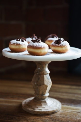 Delicious chocolate topped donuts on a vintage cake stand in a restaurant - Australian Stock Image