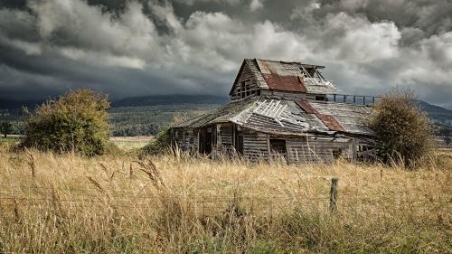 Derelict farmhouse in a paddock with dramatic sky in Tasmania