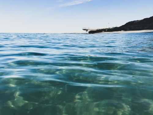 Deserted Ocean in foreground with jetty in background on calm clear sky day - Australian Stock Image