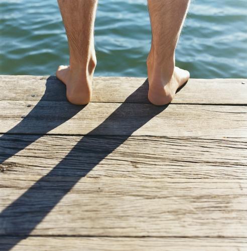 Detail of feet standing on wooden jetty with water in background