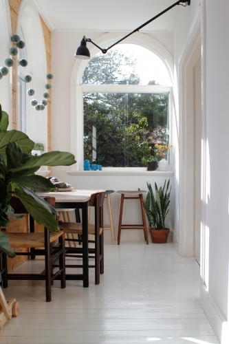 Dining table with chairs in sun room with arched windows, stools and plants