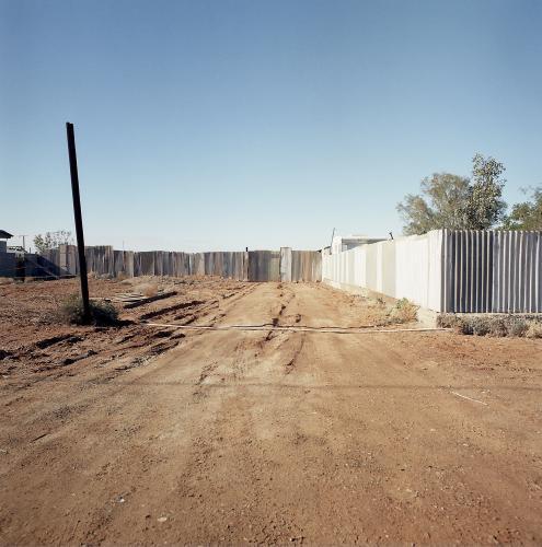 Dirt road in remote town with metal fence - Australian Stock Image