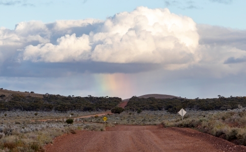 dirt road with storm clouds and rainbow on horizon - Australian Stock Image