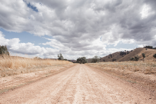 Dirt track with dry, summer grasses and cloudy sky - Australian Stock Image