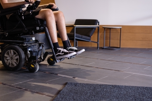disabled man in motorised wheelchair, in foyer of apartment building - Australian Stock Image
