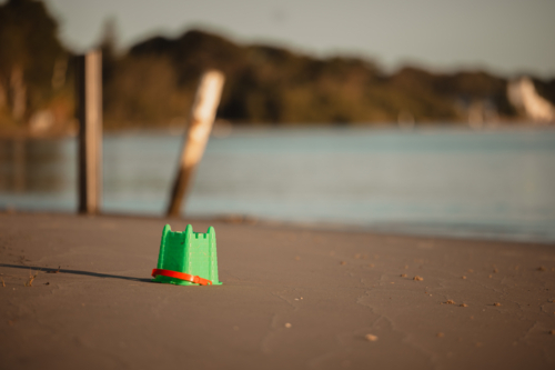 Discarded children's sand castle bucket on the beach at sunset - Australian Stock Image