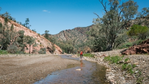 Distant figure standing in a creek in a remote rocky landscape - Australian Stock Image