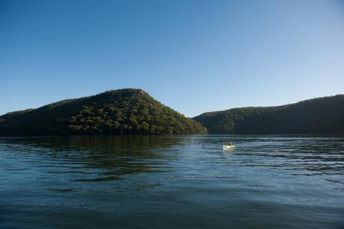 Distant man kayaking on lake with mountain view - Australian Stock Image
